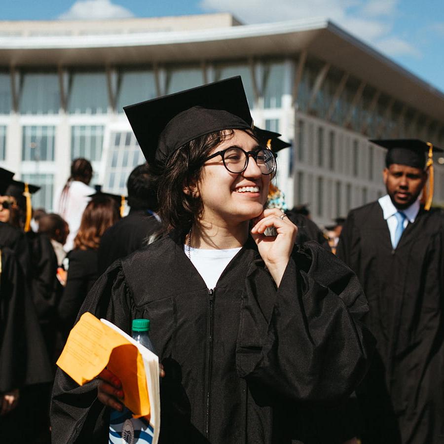 Student in cap & gown at commencement on Campus Center lawn.